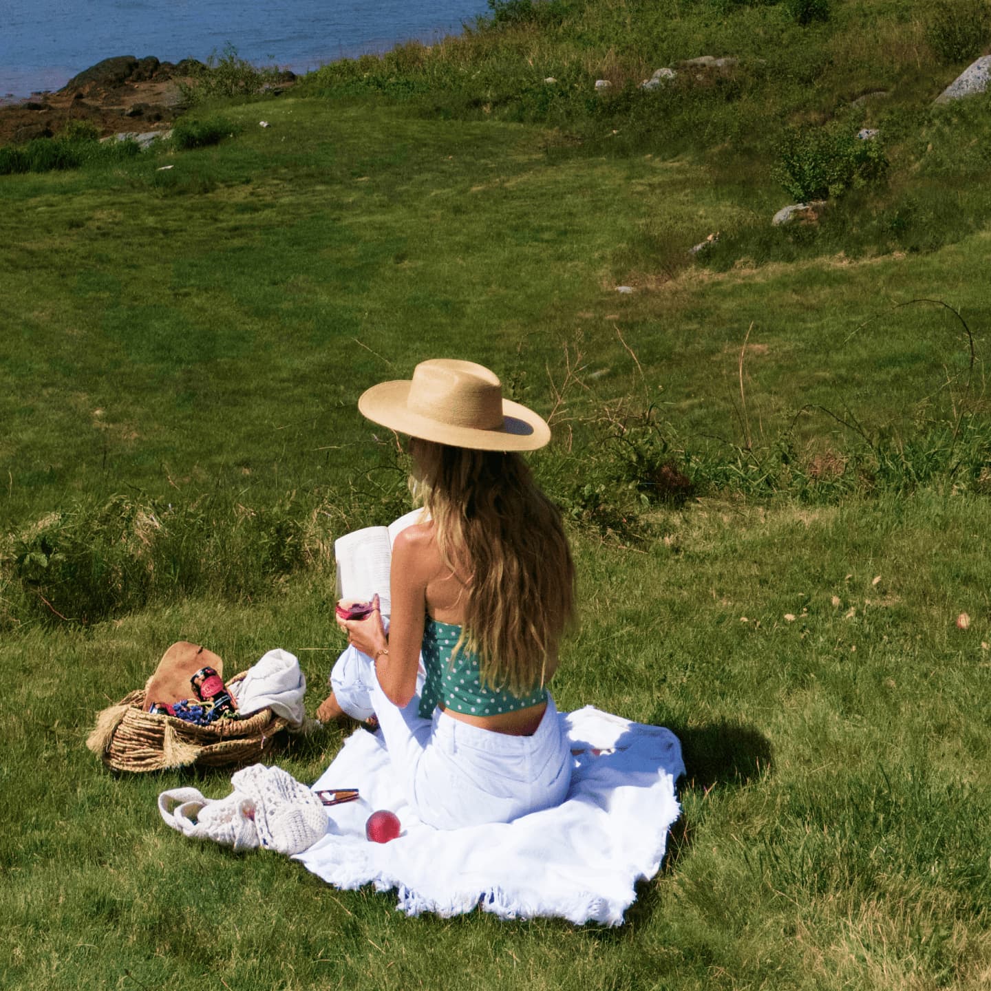 Woman wearing hat reading in the sun by a body of water